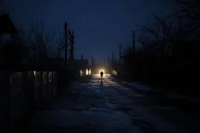 A man is silhouetted in the headlights of a car during a blackout in the town of Kolychivka, Ukraine, Wednesday, February 1, 2023. (Photo by Daniel Cole/AP Photo)