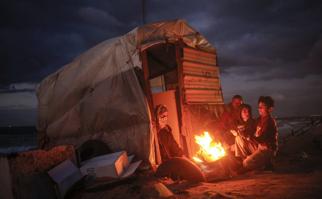 Palestinian children warm up around a fire by a shack along the beach in Gaza City on November 22, 2017. (Photo by Mohammed Abed/AFP Photo)