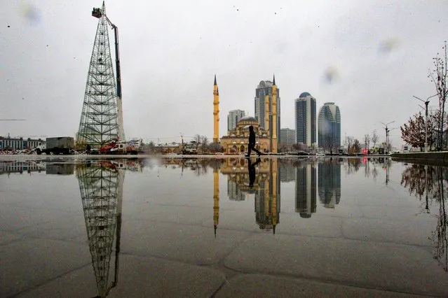 A man walks through a square after snowfall as workers assemble a Christmas tree, with the main Mosque and skyscrapers in the background in downtown Grozny, the capital of Chechnya, Russia, Sunday, December 6, 2020. (Photo by Musa Sadulayev/AP Photo)