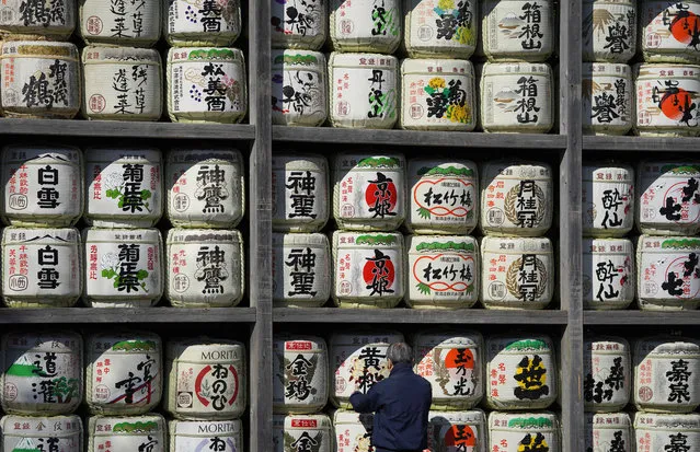A visitor watches a display of barrels of sake, or rice wine, dedicated to Tsurugaoka Hachimangu shrine in the compound of the Shinto shrine in Kamakura, southwest of Tokyo, Sunday, February 4, 2018. Kamakura is one of popular tourist spots with Zen temples and Shinto shrines. (Photo by Shizuo Kambayashi/AP Photo)