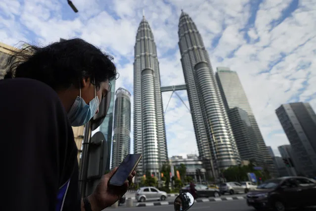 A man wearing a face mask listens to live broadcast in front of Twin Towers in downtown Kuala Lumpur, Malaysia, Monday, January 11, 2021. Prime Minister Muhyiddin Yassin says Malaysia’s health care system is at a breaking point as he announced new movement curbs, including near-lockdown in Kuala Lumpur and several high-risk states to rein in a spike in coronavirus cases. (Photo by Vincent Thian/AP Photo)
