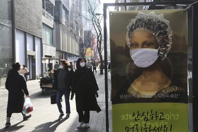 People wearing face masks to help protect against the spread of the coronavirus walk by an advertisement for a hair shop along a shopping street in Seoul, South Korea, Sunday, January 31, 2021. (Photo by Ahn Young-joon/AP Photo)