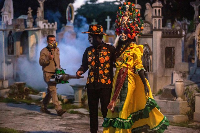A health worker dispense insecticide with fogging machines to kill mosquitoes spreading dengue fever in front of a couple dressed as “catrinas” ahead of the Day of the Dead celebrations in Merida, Yucatan, Mexico on October 23, 2024. (Photo by Hugo Borges/AFP Photo)