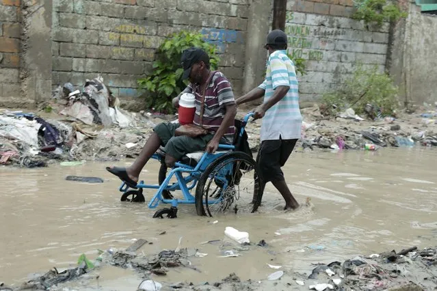 A man in a wheelchair is helped to make his way through a flooded street after a heavy rain, in Port-au-Prince, Haiti, Saturday, June 3, 2023. (Photo by Joseph Odelyn/AP Photo)