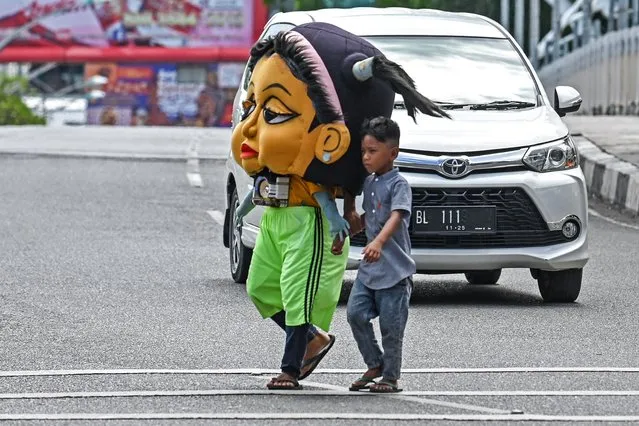 A man wearing a headgear walks along with his child on a street in Banda Aceh on July 25, 2023. (Photo by Chaideer Mahyuddin/AFP Photo)