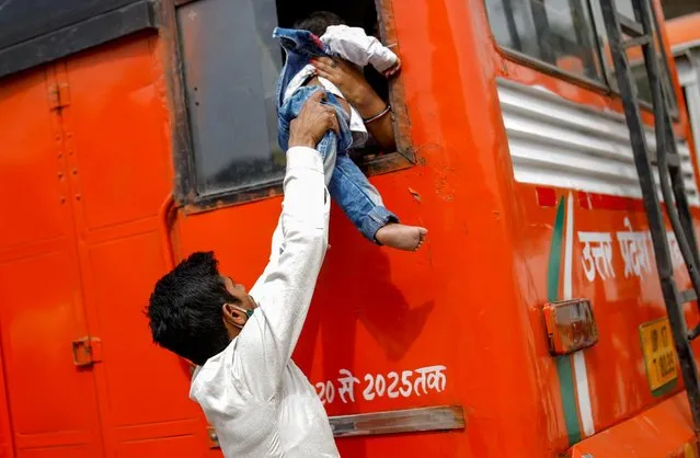 A migrant worker passes his son through a bus window as they return to their village in Ghaziabad on the outskirts of New Delhi, India, April 20, 2021. Migrant workers were fleeing Delhi by the busload amid a six-day lockdown in the capital to curb the latest surge in coronavirus cases in India. (Photo by Adnan Abidi/Reuters)