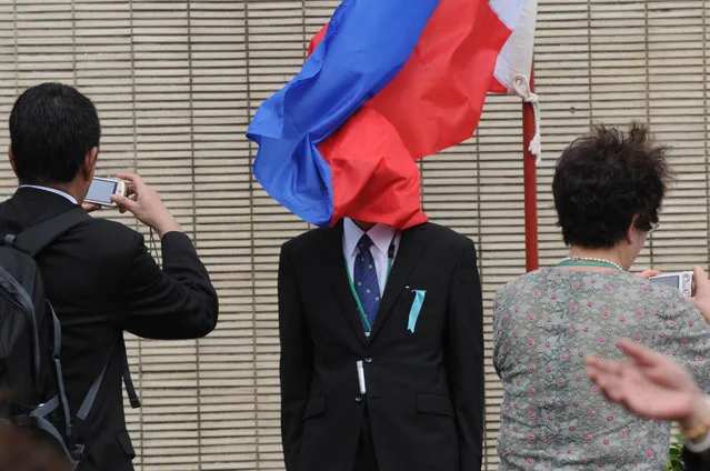 The wind blows the Philippine flag across the face of a man as relatives of fallen Japanese soldiers have their photos taken during a ceremony at a war memorial in Laguna province, Philippines on January 29, 2016. The emperor and empress of Japan are in the Philippines for a four-day visit coinciding with the 60th anniversary of the normalisation of relations between Japan and the Philippines after the second world war. (Photo by George Calvelo/Barcroft India)