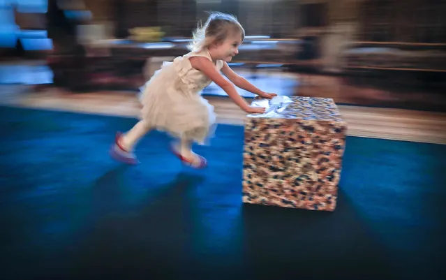 In this Tuesday, December 13, 2016 photo taken with a slow shutter speed, 3 year old Nicole pushes her present box, after a Christmas show for children of Romanian military families, in Bucharest, Romania. Romania's defense ministry has laid on a Christmas show for dozens of Romanian children whose fathers were killed or injured serving in international peacekeeping missions at the National Military Circle, a grand 19th-century building in downtown Bucharest. (Photo by Vadim Ghirda/AP Photo)
