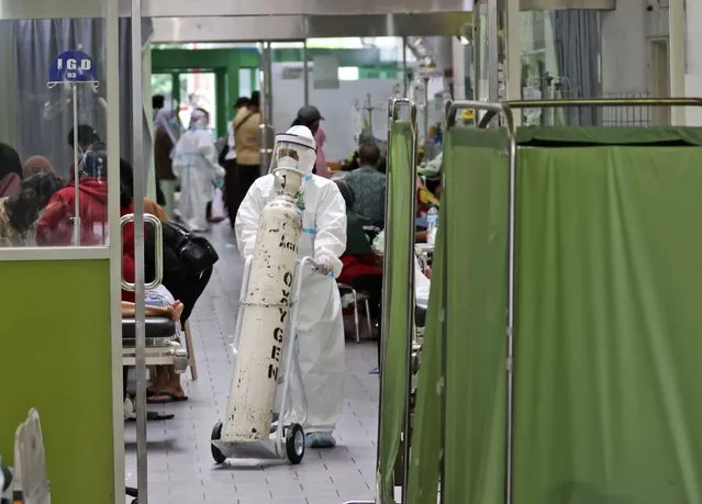 A paramedic pushes an oxygen tank at the emergency ward of an overcrowded hospital amid COVID-19 cases, in Surabaya, East Java, Indonesia, Friday, July 9, 2021. The world's fourth most populous country is running out of oxygen as it endures a devastating wave of coronavirus cases and the government is seeking emergency supplies from other countries, including Singapore and China. (Photo by Trisnadi/AP Photo)