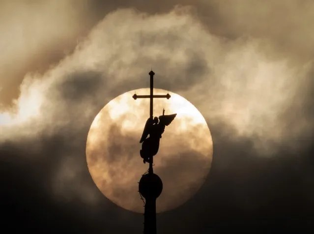 The city landmark weather vane in the form of an Angel, fixed atop a spire of the Saints Peter and Paul Cathedral, is silhouetted against the sun in the clouds in St. Petersburg, Russia, Thursday, June 24, 2021. (Photo by Dmitri Lovetsky/AP Photo)