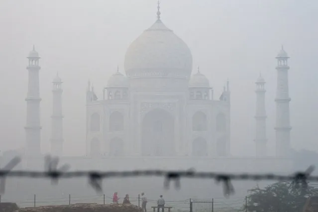 Tourists sit against the backdrop of Taj Mahal amid smoggy conditions in Agra on November 7, 2023. (Photo by Pawan Sharma/AFP Photo)