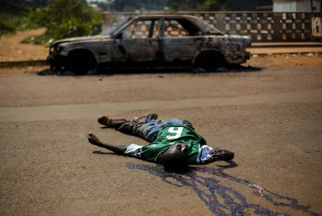 The body of a man suspected to be an ex-Seleka militiaman lies by a charred car in Bangui, Central African Republic, on December 20, 2013. After a period of relative calm, violence has flared anew in the Central African Republic with angry demonstrations against Chadian peace keepers, shoo touts at checkpoints and the destruction of a mosque. (Photo by Jerome Delay/Associated Press)