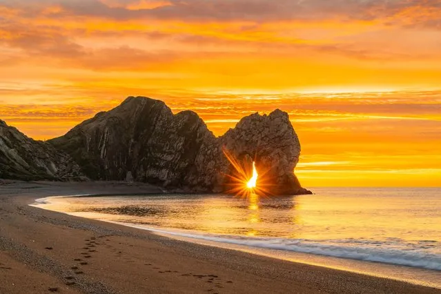 A spectacular sunrise at Durdle Door in Dorset, UK on November 22, 2023, as the clouds glow orange above the famous limestone rock sea arch. (Photo by Graham Hunt/Alamy Live News)