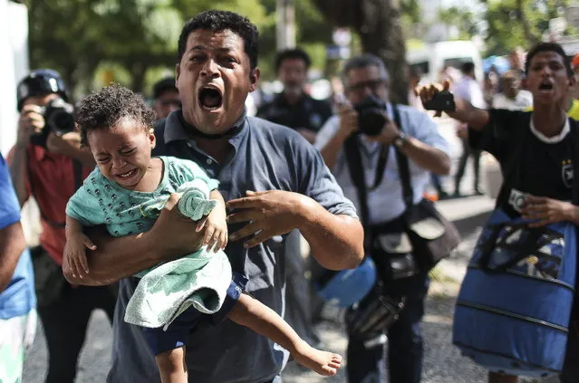 A man runs carrying his daughter during a forced eviction by police from a building that belongs to the soccer club Flamengo, in Rio de Janeiro, Brazil, April 14, 2015. Weeks ago a group of homeless people occupied the building. After their eviction, they expect now a housing solution by government. (Photo by Antonio Lacerda/EPA)