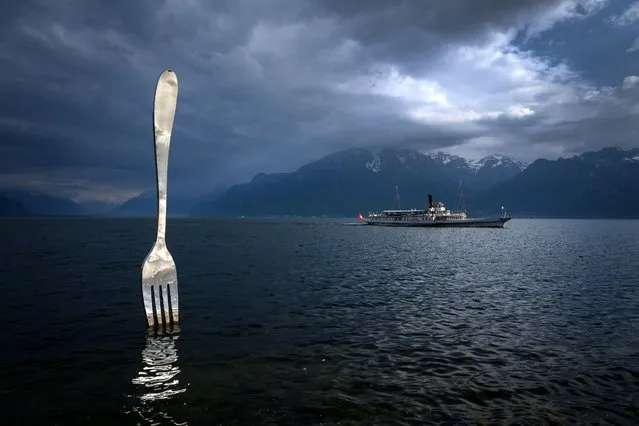 A picture taken on May 21, 2019 in Vevey shows the paddle steamer “Italie” of the Compagnie Generale de Navigation sur le lac Leman, commonly abbreviated to CGN, sailing on Lake Geneva past a giant fork sculpture designed by Switzerland's artist Jean-Pierre Zaugg. (Photo by Fabrice Coffrini/AFP Photo)