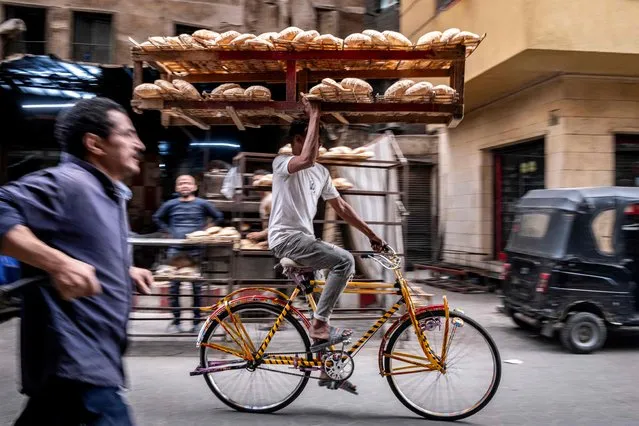A deliveryman balances a tray of freshly baked bread while riding his bicycle along the al-Darb al-Ahmar district in the old quarters of Cairo on March 6, 2024. (Photo by Amir Makar/AFP Photo)