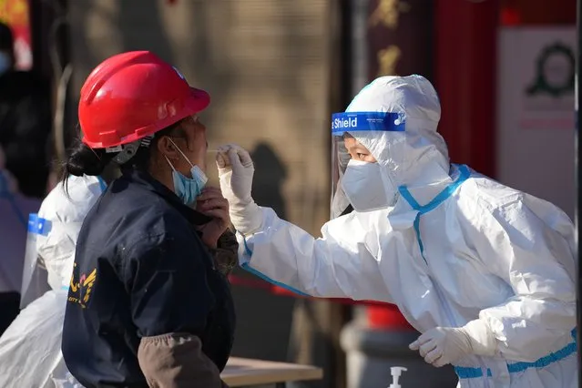 In this photo released by China's Xinhua News Agency, a worker wearing a protective suit collects a throat swab sample at a COVID-19 testing site in Xi'an in northwestern China's Shaanxi Province, Tuesday, December 21, 2021. China on Wednesday ordered millions of people locked down in neighborhoods and workplaces in the northern city of Xi'an following a spike in coronavirus cases. (Photo by Li Yibo/Xinhua via AP Photo)