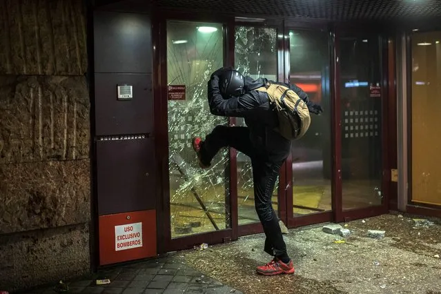 A demonstrator smashes the front entrance of a bank office during a protest against the government in Madrid, Spain, Saturday, March 22, 2014. Spanish police and protesters clashed during an anti-austerity demonstration that drew tens of thousands of people to central Madrid on Saturday. Police said in a statement six officers were injured and 12 people were arrested. (Photo by Andres Kudacki/AP Photo)