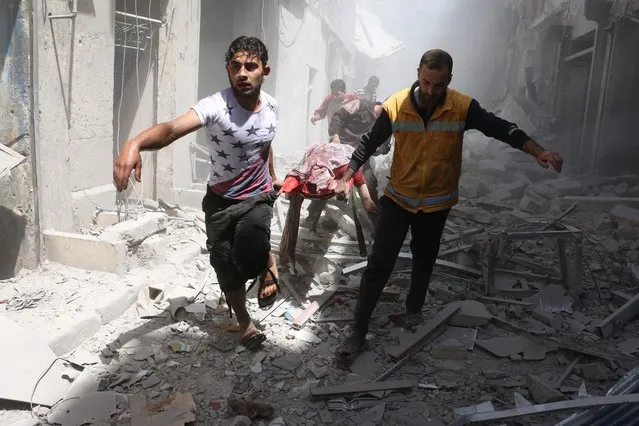 Syrian men carry a body on a stretcher amid the rubble of destroyed buildings following a reported air strike on the rebel-held neighbourhood of Al-Qatarji in the northern Syrian city of Aleppo, on April 29, 2016. Fresh bombardment shook Syria's second city Aleppo, severely damaging a local clinic as outrage grows over an earlier air strike that destroyed a hospital. The northern city has been battered by a week of air strikes, rocket fire, and shelling, leaving more than 200 civilians dead across the metropolis. The renewed violence has all but collapsed a fragile ceasefire deal that had brought an unprecedented lull in fighting since February 27. (Photo by Ameer Alhalbi/AFP Photo)