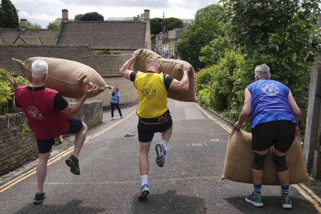 Participants pick up the Woolsacks on their shoulders during the annual Tetbury Woolsack Races in Tetbury, Gloucestershire, England, Monday, May 27, 2024. The annual Woolsack Races that take place in the Wiltshire wool-town of Tetbury. Every year teams of men, women and children carry sacks of British wool, 60-pound (27 kg) for men's races and 35 pounds (16 kg) for women's, up and down the Gumstool Hill with course of 240 yards (220 meters). An official Woolsack Races has been going since 1972, with world records entered in the “Guinness Book of Records”. (Photo by Kin Cheung/AP Photo)