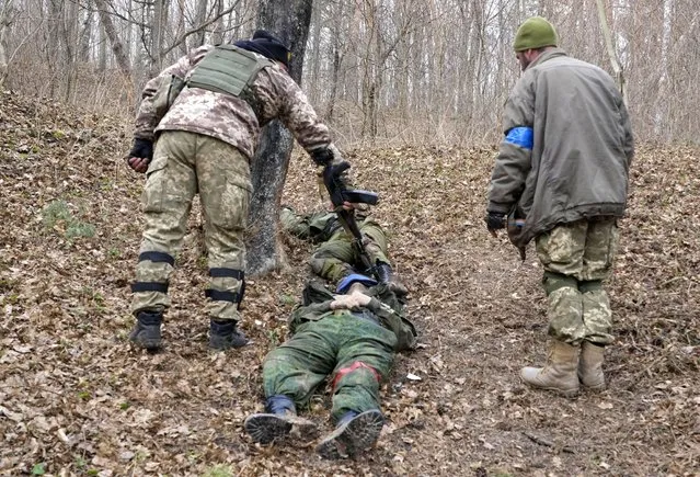 Ukrainian soldiers look over the bodies of dead Russian soldiers after recent fights in the town of Trostsyanets, some 400km (250 miles) east of capital Kyiv, Ukraine, Monday, March 28, 2022. The more than month-old war has killed thousands and driven more than 10 million Ukrainians from their homes including almost 4 million from their country. (Photo by Efrem Lukatsky/AP Photo)