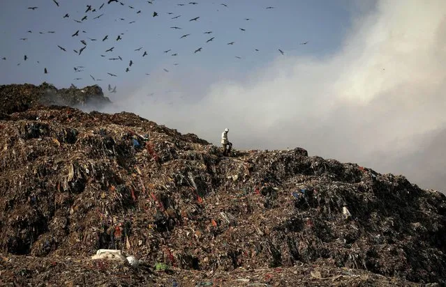 A man walks past burning garbage at the Ghazipur landfill site in New Delhi, India, March 28, 2022. (Photo by Adnan Abidi/Reuters)