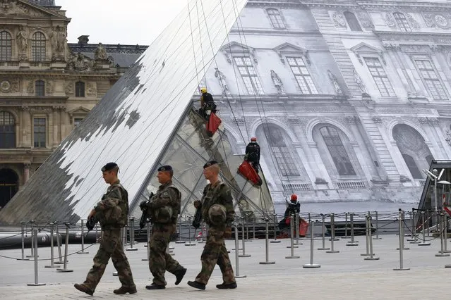 French soldiers patrol as rope access technicians work on the Louvre Pyramid as part of JR project in Paris, Tuesday, May 24, 2016. (Photo by Francois Mori/AP Photo)