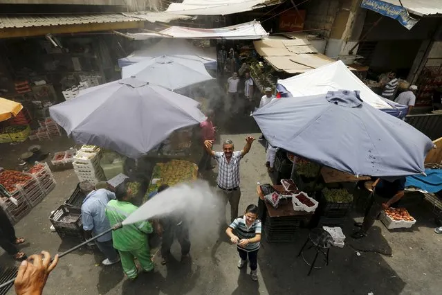 Residents react react as Greater Amman Municipality personnel spray them with a water sprinkler in order to cool them down as part of measures to ease the effect of a heatwave, in Amman, Jordan, August 3, 2015. (Photo by Muhammad Hamed/Reuters)