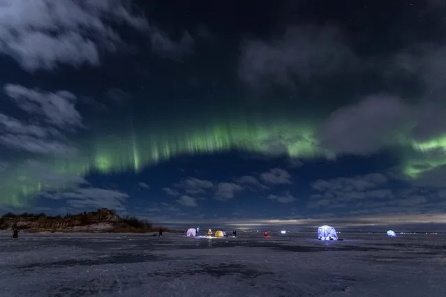 The northern lights, or aurora borealis, illuminate the night sky above fishermen on the ice of Finnish Gulf outside St. Petersburg, Russia, Saturday, January 15, 2022. (Photo by Ivan Petrov/AP Photo)