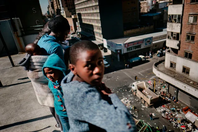 Residents look from a terrace at municipal workers clearing the belongings of evicted residents of the Fattis Mansion in Johannesburg, on July 21, 2017. Residents of the allegedly illegally occupied building were forcibly removed by dozens of red clad security men and their belongings laid on the pavement outside the building. Several buildings in the central district of Johannesburg are illegally occupied by a large number of residents, often migrants, who live in substandard conditions. (Photo by Marco Longari/AFP Photo)