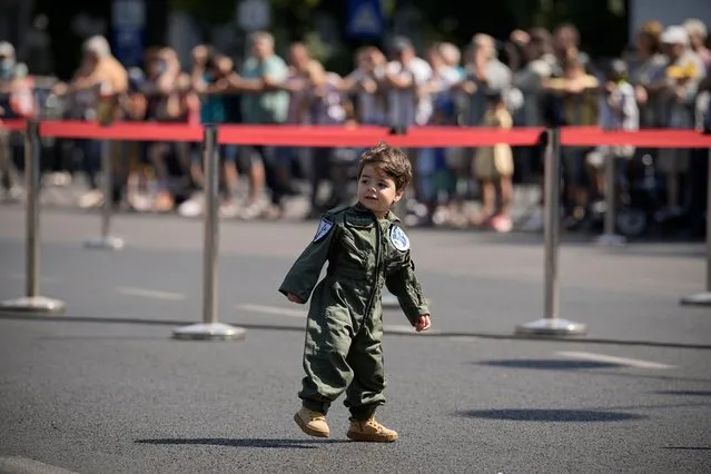 Aaron, two years old, wears a fighter pilot uniform replica before a military ceremony at the Aviation Heroes monument in Bucharest, Romania, Wednesday, July 20, 2022. A ceremony and flyover by Romanian and NATO airplanes took place to mark Aviation Day next to the monument that celebrates aviators, both military and civilian, that lost their lives in the line of duty. (Photo by Vadim Ghirda/AP Photo)