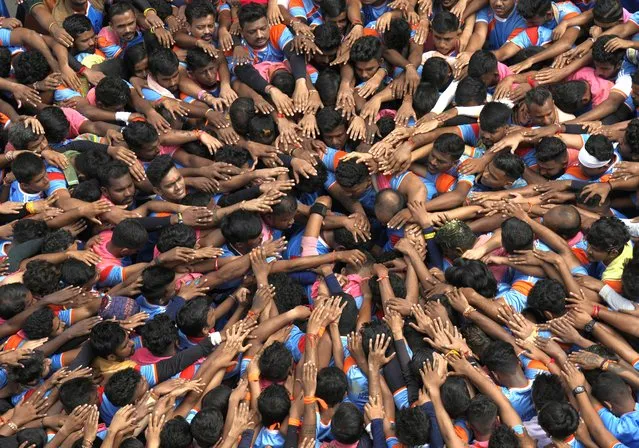 People pray before forming a human pyramid to break the “Dahi handi”, an earthen pot filled with curd, as part of celebrations to mark Janmashtami festival in Mumbai, India, Friday, August 19, 2022. The festival marks the birth of Hindu god Krishna and the act seeks to reenact the story of Lord Krishna stealing butter during his childhood. (Photo by Rajanish Kakade/AP Photo)
