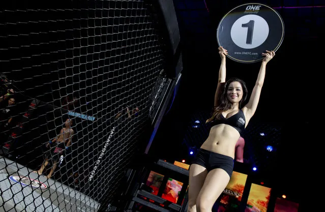 In this Saturday, July 18, 2015, photo, a ring girl walks at the beginning of the lethwei featherweight match - a Myanmar traditional martial art which practices a rough form of kickboxing – between Tha Pyay Nyo, left, and Hlit Hlit Lay, at a mixed-martial-arts “One Championship” event broadcast globally on cable television networks, in Yangon, Myanmar. (Photo by Gemunu Amarasinghe/AP Photo)