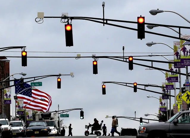 A flag waves in gusty winds as pedestrians cross the street in Newark, New Jersey, on September 18, 2012. A tornado watch was issued for parts of New Jersey, New York City and New York's lower Hudson Valley. (Photo by Julio Cortez/Associated Press)