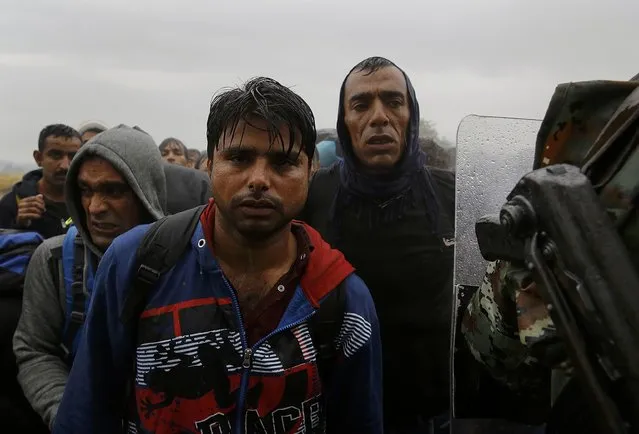 An armed Macedonian soldier (R) stands in front of migrants and refugees in an attempt to control a crowd waiting to cross the border line from Greece into Macedonia, during a rainstorm near the Greek village of Idomeni, September 10, 2015. (Photo by Yannis Behrakis/Reuters)