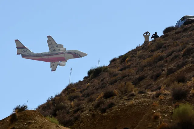 An RJ85 air tanker flies by people looking from the top of a hill at a wildfire on Sunday, August 7, 2016, in Hesperia, Calif. (Photo by David Pardo/The Daily Press via AP Photo)