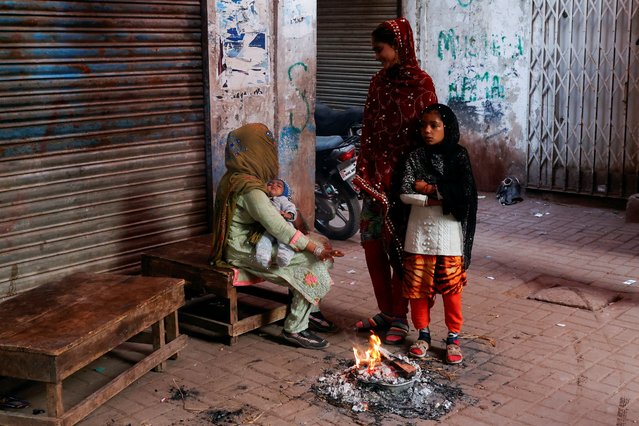 A woman and her children keep themselves warm near a fire on a cold winter morning along a street in Karachi, Pakistan on December 27, 2024. (Photo by Akhtar Soomro/Reuters)