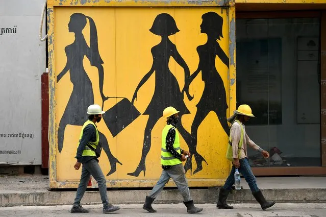 Construction workers walk past a mural in Phnom Penh on September 6, 2022. (Photo by Tang Chhin Sothy/AFP Photo)