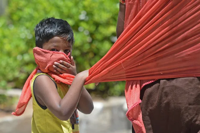 In this picture taken on July 8, 2020, a boy covers his face with the scarf of his mother as he walks along the road after the government eased a nationwide lockdown imposed as a preventive measure against the COVID-19 coronavirus, in Chennai. India on July 6 became the country with the third-highest coronavirus caseload in the world, as a group of scientists said there was now overwhelming evidence that the disease can be airborne – and for far longer than originally thought. (Photo by Arun Sankar/AFP Photo)