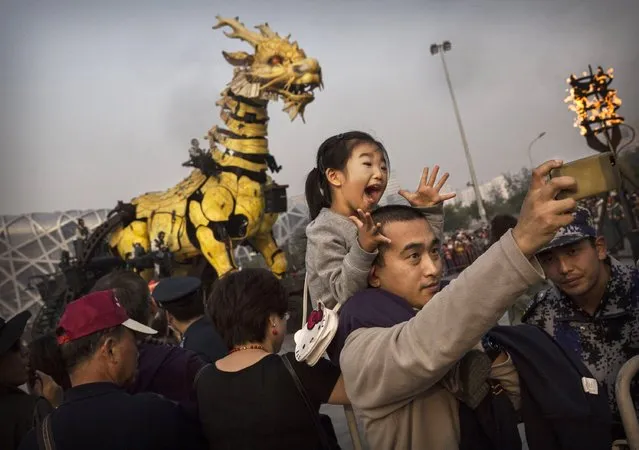 A Chinese girl reacts as her father takes a picture of them in front of a large mechanical dragon called “Dragon Horse” that is part of the Long Ma Performance by the French company La Machine at the National Stadium on October 18, 2014 in Beijing, China. The event was held to mark 50 years of diplomatic relations between France and China. (Photo by Kevin Frayer/Getty Images)