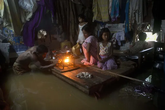 A man lights a stove to make food as his family members take shelter on a bed after flood waters enter their house following heavy monsoon rains in Gauhati, India, Wednesday, September 23, 2015. India receives its monsoon rains from June to September. (Photo by Anupam Nath/AP Photo)