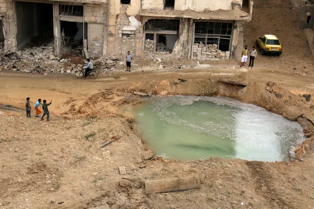 People inspect a hole in the ground filled with water in a damaged site after airstrikes on the rebel held Tariq al-Bab neighbourhood of Aleppo, Syria September 23, 2016. (Photo by Abdalrhman Ismail/Reuters)