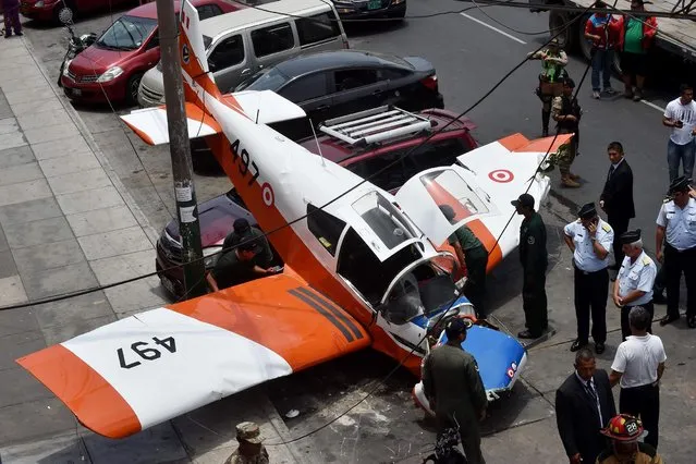Fire fighters, police officers and members of the Air Force are at the scene where a Peruvian Air Force training plane crashed on a street in Lima on February 4, 2019. The crash left one of two occupants of the plane injured and damaged several parked vehicles in a neighborhood a few blocks away from an Air Force base. (Photo by Cris Bouroncle/AFP Photo)