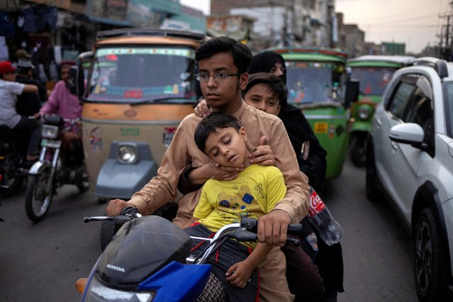A boy sleeps in the arms of family members as they navigate traffic on a motorbike along Hussain Agahi Road in Multan, Pakistan on May 28, 2025. (Photo by Adrees Latif/Reuters)