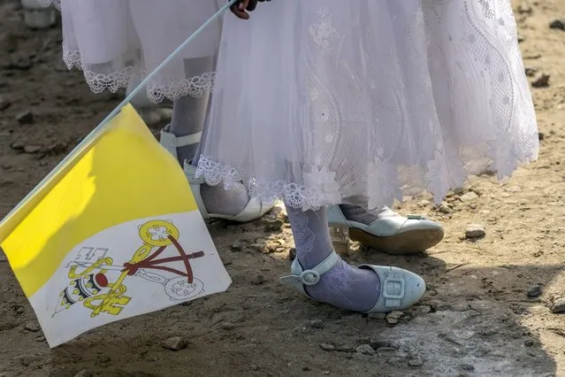 A young girl holds a Vatican flag and rocks on her shoes after standing for a long time prior to the arrival of Pope Francis at the St. Theresa Cathedral in Juba, South Sudan, Saturday, February 4, 2023. (Photo by Ben Curtis/AP Photo)