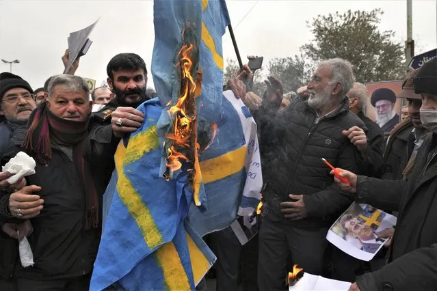 Protesters burn representations of the Swedish flag during a protest to denounce the recent desecration of Islam's holy book, Quran, by a far-right activist in Sweden, after Friday Prayers in Tehran, Iran, Friday, January 27, 2023. (Photo by Vahid Salemi/AP Photo)