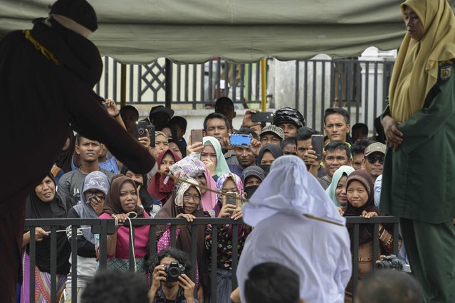 People watch as Tjia Nyuk Hwa, 45, an Indonesian Christian, is publicly flogged outside a mosque in Banda Aceh on February 27, 2018, for playing a children' s entertainment game seen as violating Islamic law. (Photo by Chaideer Mahyuddin/AFP Photo)