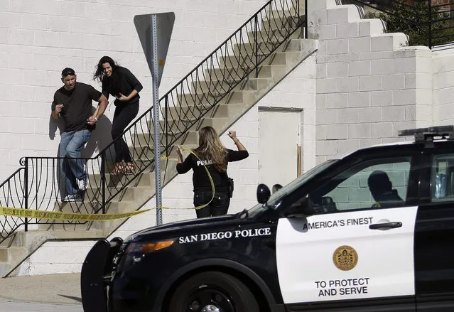 San Diego police officers assist a couple as they evacuate a building in San Diego on Wednesday, November 4, 2015. A man with a high-powered gun was firing sporadically inside a San Diego apartment complex, causing the city's nearby airport to stop planes from landing, authorities said. (Photo by Gregory Bull/AP Photo)
