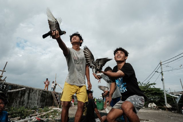 Two men hold female pigeons, fluttering them to attract male pigeons flying from a distance, for fun in Cilincing, North Jakarta, on September 20, 2025. (Photo by Yasuyoshi Chiba/AFP Photo)