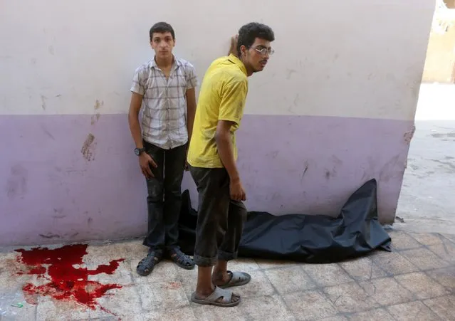 Syrian men stand next to a body bag in front of a makeshift hospital in the Tariq al-Bab neighbourhood of Aleppo, following reported air raids that targetted rebel-held areas in the northern city on August 16, 2016. Air raids on two rebel-held districts of Syria's battleground second city Aleppo killed 19 civilians, including three children, a monitoring group said. (Photo by Thaer Mohammed/AFP Photo)